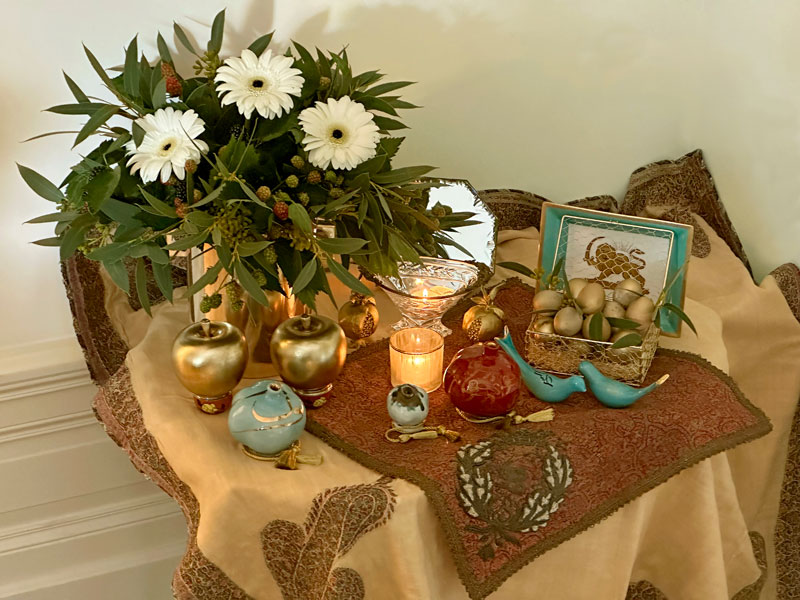 A mirror, tea lights, sculptured apples, pomegranates and birds, as well as decorated eggs, all presented on antique Persian textiles