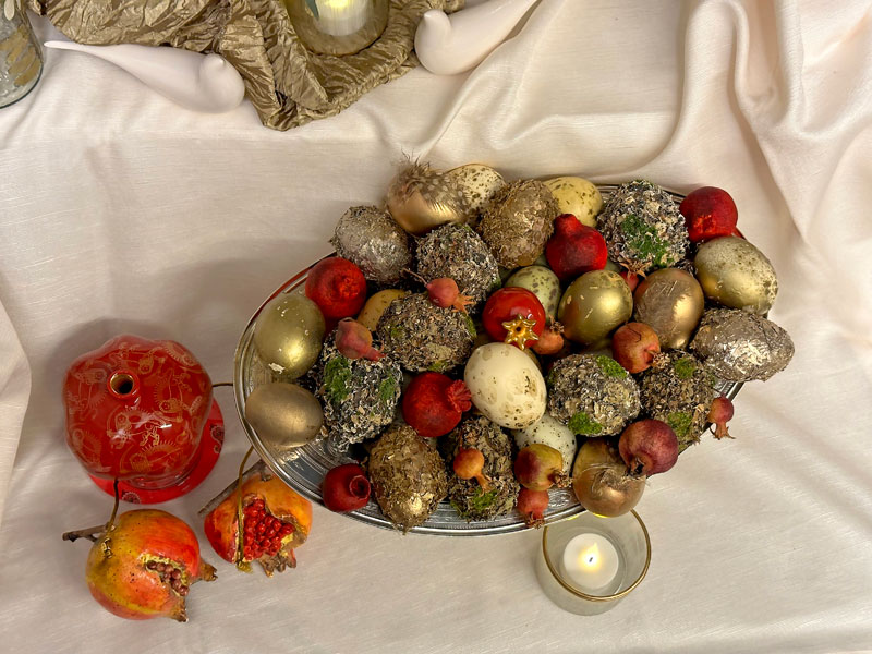 An antique silver vessel contains a variety of tastefully decorated eggs in gold and green tones