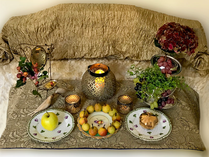 Sofreh elements include a mirror, flames, statuettes of birds, gilded coins, apples and pomegranates