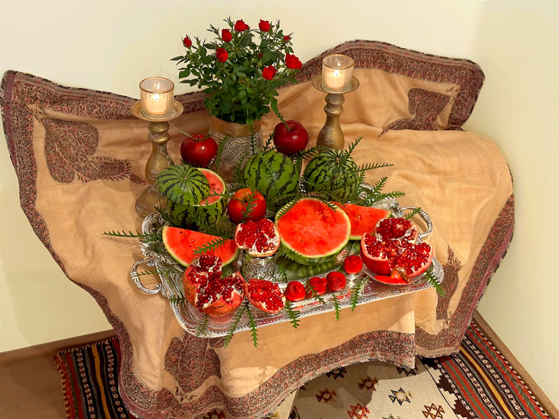 pot of red miniature roses and an attractive display of red fruits, presented on an antique silver-plated tray atop an antique Persian textile in silk