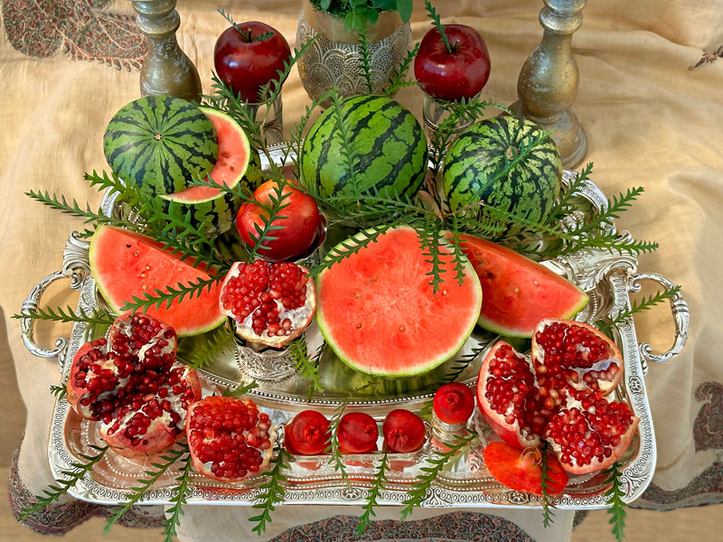 Shiny red apples, miniature whole and cut watermelons, sculptured and fresh open pomegranates, all embellished with sprigs of foliage
