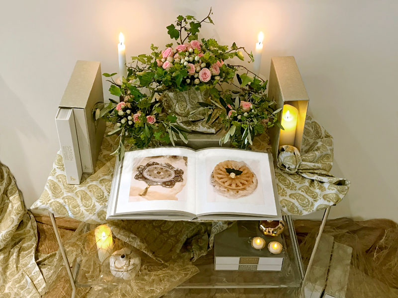 several volumes of the book with delicate bouquets of spray roses and foliage and lengths of fine textiles